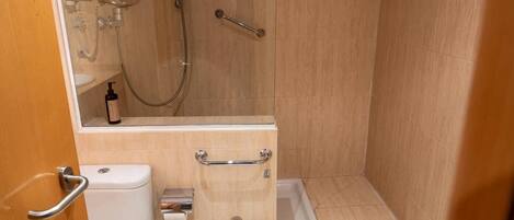 A bathroom with a shower, toilet, and sink, equipped with grab bars and a handheld showerhead.