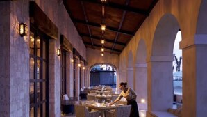 A restaurant with tables set for dining, a waiter attending to guests, and a view of the outdoors through an arched window. - LUXURY STUDIO 5 🎖️, A PARADISIAC PLACE, IN FRONT OF THE SEA  (Cabo San Lucas)