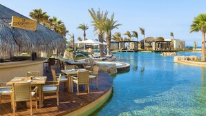 A resort pool area with lounge chairs, a bar, and thatched-roof structures. - LUXURY STUDIO 5 🎖️, A PARADISIAC PLACE, IN FRONT OF THE SEA  (Cabo San Lucas)