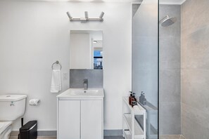 A modern bathroom with a glass-enclosed shower, a white sink, and a mirror above the sink. - Pastel Apartments (Miami)