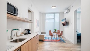 A modern kitchen with a microwave, coffee maker, and sink. There is a dining area with a table and chairs, and a large window providing natural light. - Pastel Apartments (Miami)