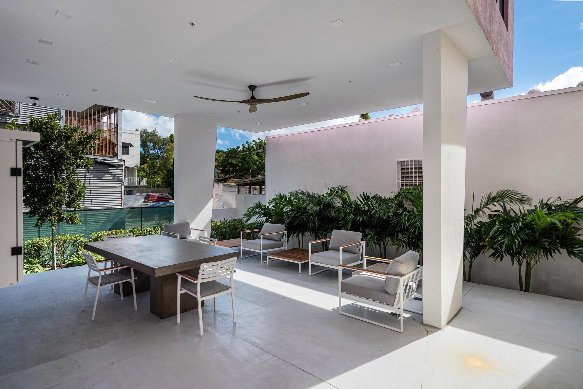 A spacious patio with a dining table and chairs, surrounded by potted plants and a view of a swimming pool.