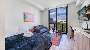 A modern bedroom with a bed, a sofa, a desk, and a balcony with a city view. - Pastel Apartments (Miami)
