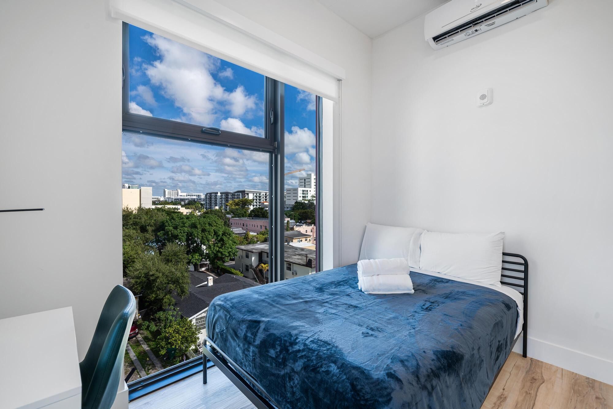 A bedroom with a large window, a bed with a blue cover, white pillows, and a black metal frame.