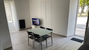 Un salon moderne avec une table à manger en verre, des chaises noires, un téléviseur à écran plat et une grande fenêtre.