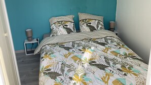 Une chambre avec des murs de couleur turquoise, une couvre-lit à motifs floraux et un luminaire suspendu.