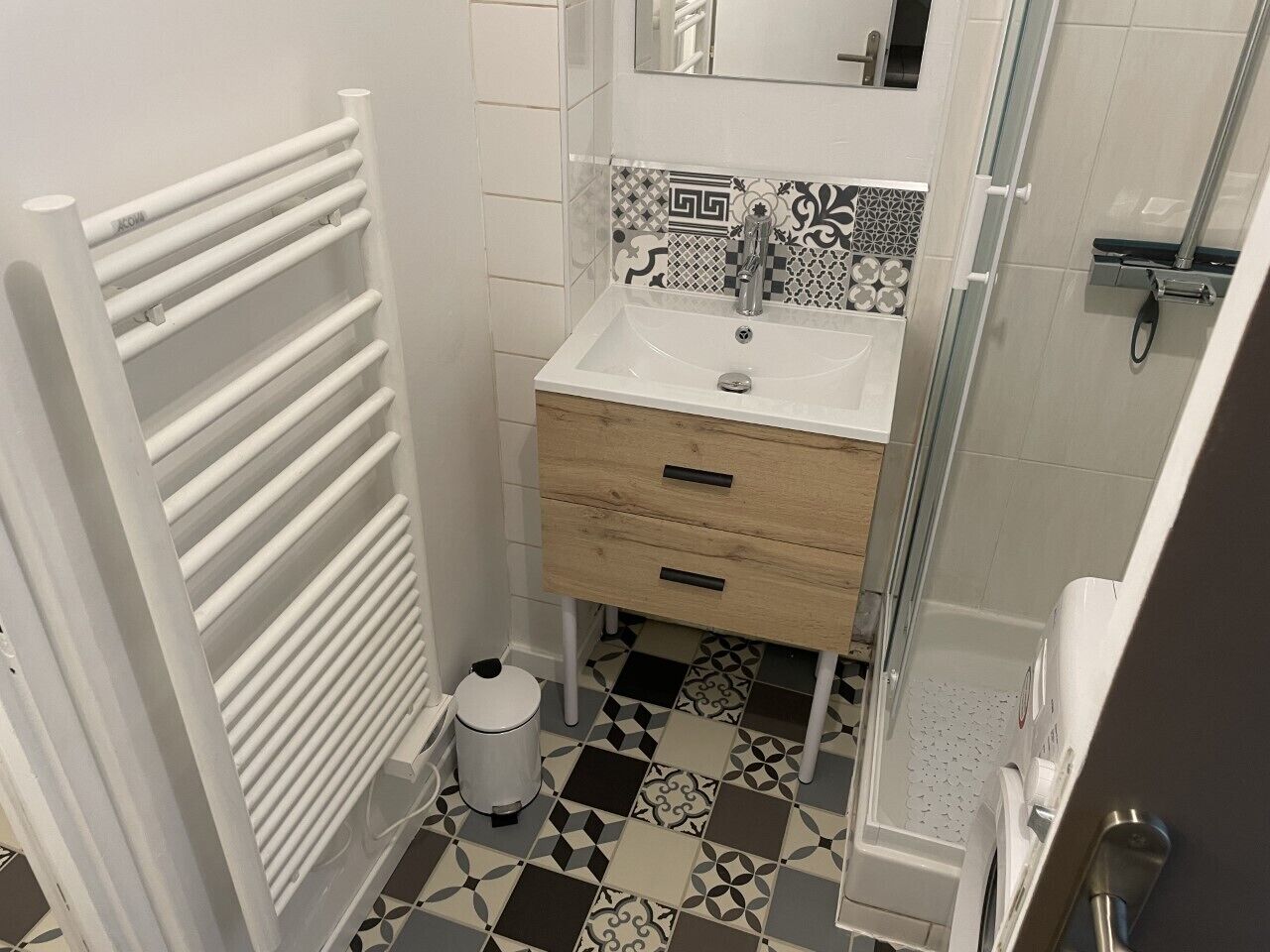 A bathroom with a white sink, a mirror, a towel rack, and patterned tiles on the floor.