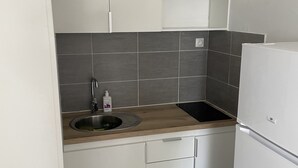 Une cuisine compacte avec des meubles blancs, un plan de travail en bois, un évier en acier inoxydable et un réfrigérateur blanc.