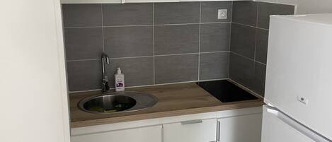 A compact kitchen with white cabinets, a wooden countertop, a stainless steel sink, and a white refrigerator.