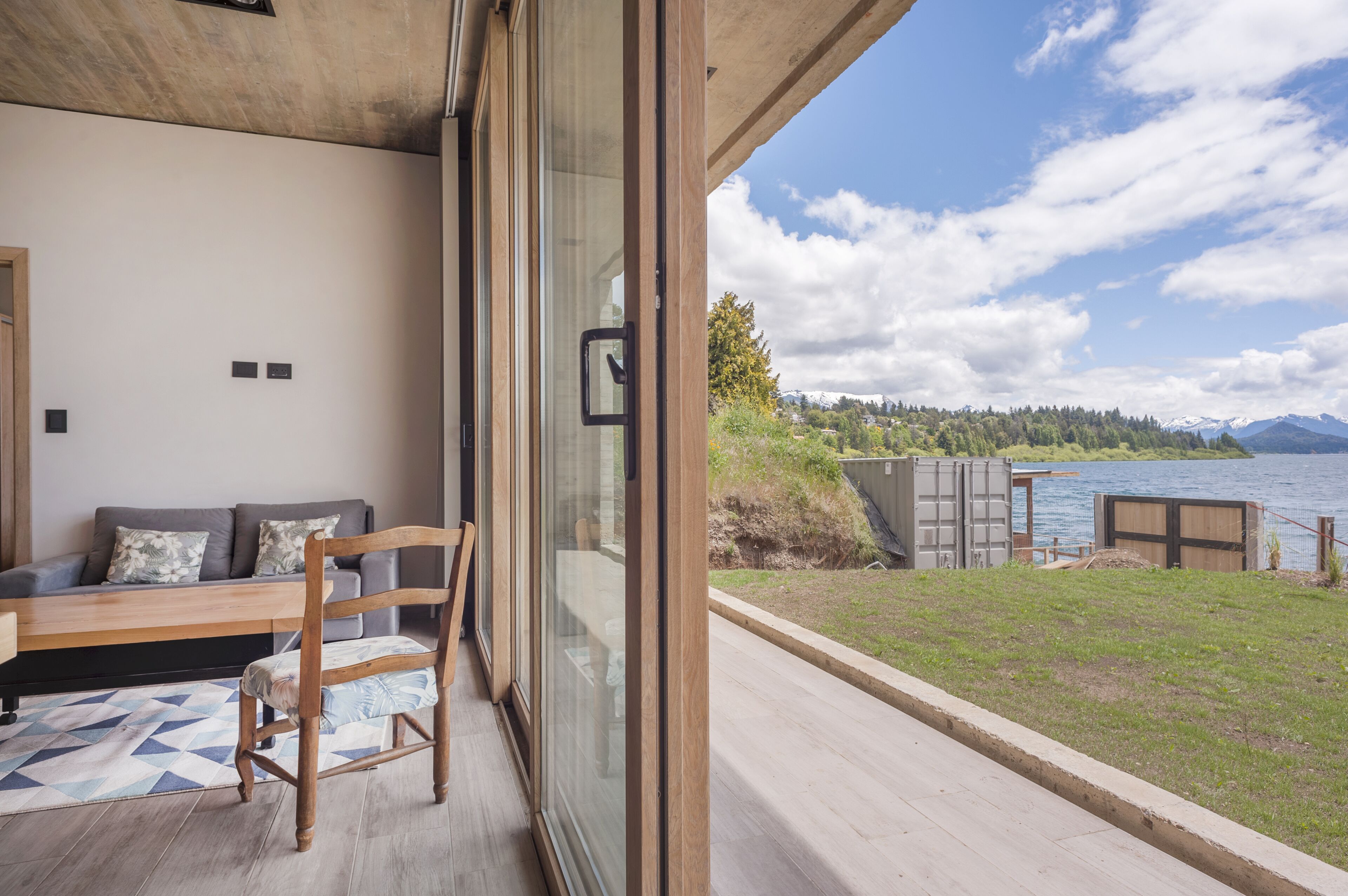 Una camera moderna con un'ampia porta scorrevole in vetro che si apre su un balcone con vista su un lago e montagne.