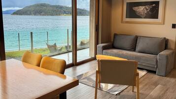 Ein modernes Interieur mit einem Holzesstisch, einem grauen Sofa und Blick auf einen See und Wald durch große Fenster.