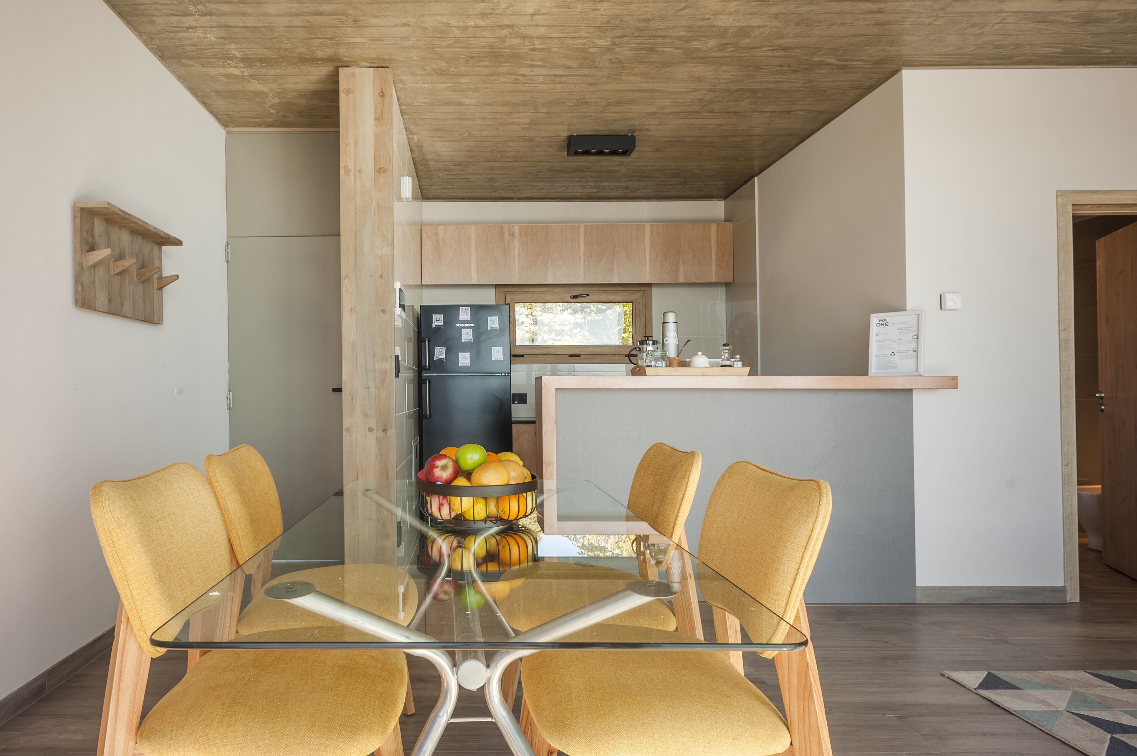 A modern kitchen with wooden cabinets, a glass dining table, and a fruit bowl.