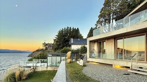 Ein modernes Küstenanwesen mit einem Betonweg, der zu einem Wintergarten mit Meerblick führt.