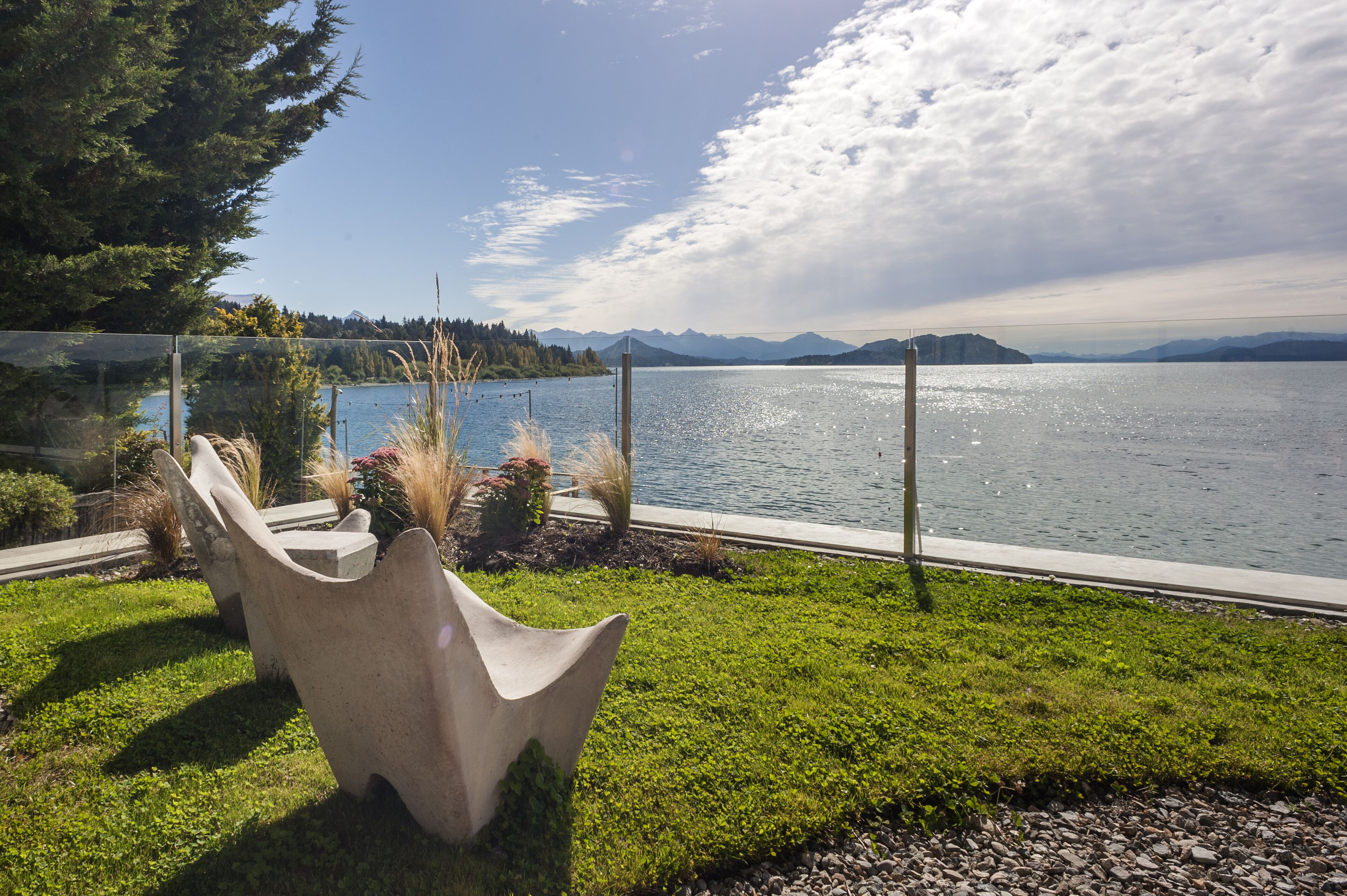 A lakeside view with a concrete sculpture, grass, and a clear sky.