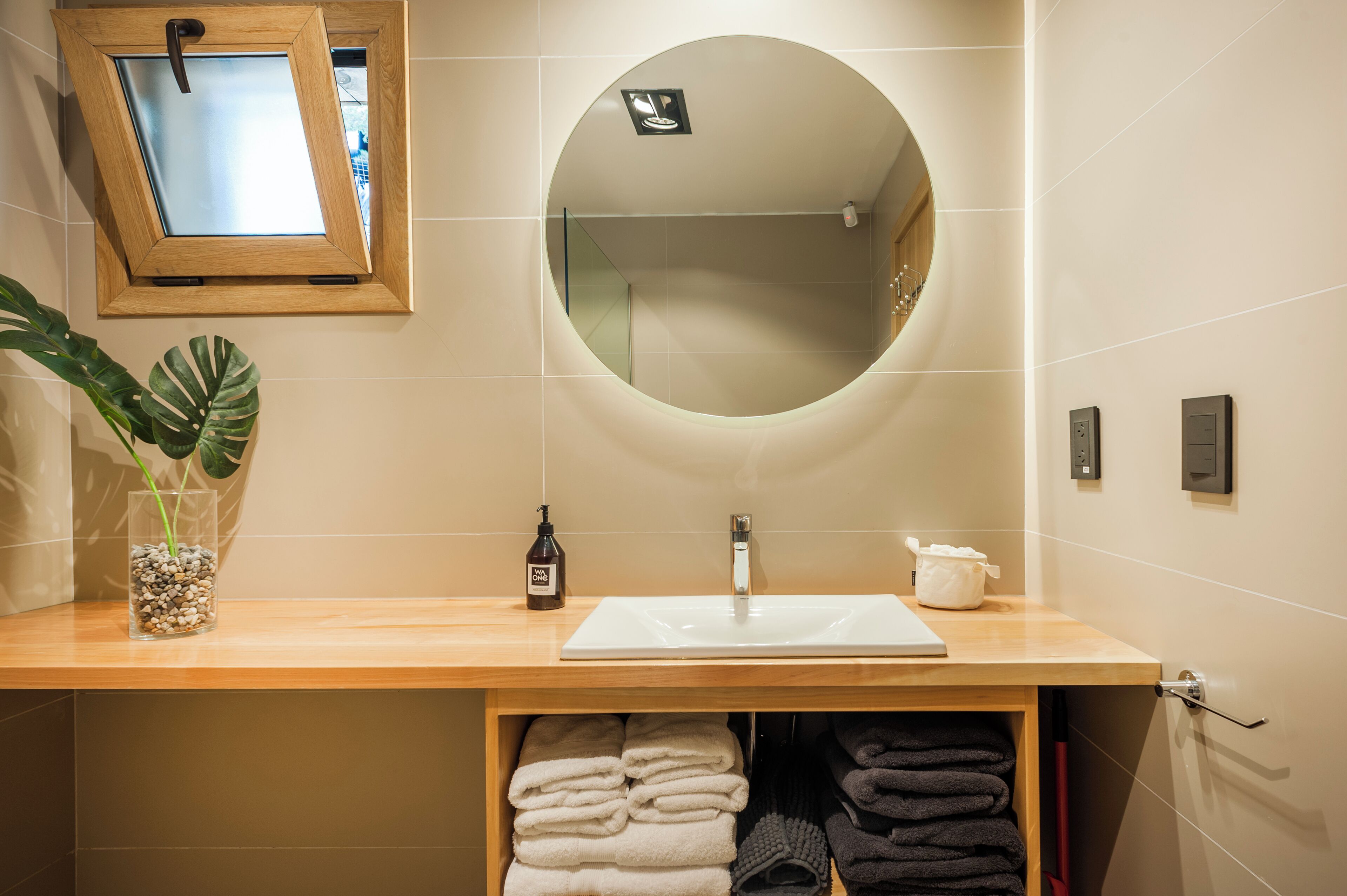 A bathroom with a wooden vanity, a round mirror, a sink, and a towel rack.