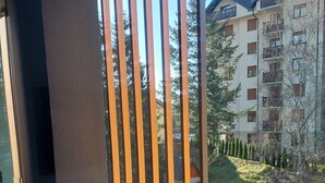 Un balcon doté de lattes en bois verticales, d’une rambarde en verre et offrant une vue sur un immeuble à plusieurs étages, lui-même agrémenté de balcons et d’un espace jardin.