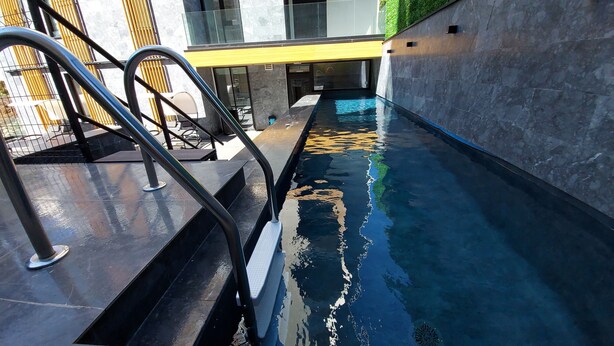 Un bâtiment moderne doté d’un espace piscine, comprenant des marches menant à une piscine entourée d’une balustrade en verre.