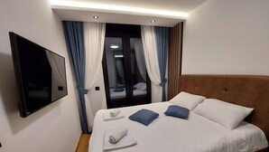 Un lit bien fait, avec des oreillers blancs et bleus, une serviette enroulée et un téléviseur à écran plat fixé au mur.