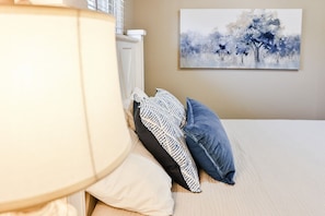 A bedroom with a bed, pillows, a lamp, and a painting on the wall.