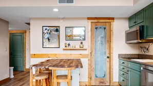 A kitchen with wooden countertops, a sink, and green cabinets. There is a wooden dining table with stools. - Stony Brook 23 | Top Floor, Heated Pool, Lake Michigan View (Glen Arbor)