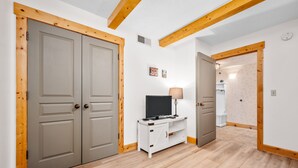 A room with two grey doors, a white entertainment unit with a TV, and wooden beams on the ceiling. - Stony Brook 23 | Top Floor, Heated Pool, Lake Michigan View (Glen Arbor)