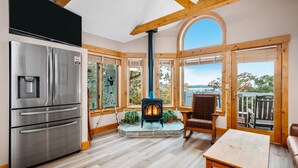 A modern kitchen with a stainless steel refrigerator, a wood-burning stove, and large windows offering a view of the outdoors. - Stony Brook 23 | Top Floor, Heated Pool, Lake Michigan View (Glen Arbor)