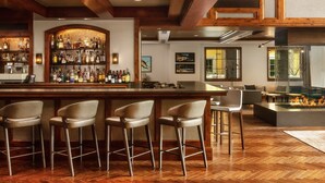 Eine Bar mit einer Holztresen, mehreren Barhocker und einer Auswahl an Flaschen.