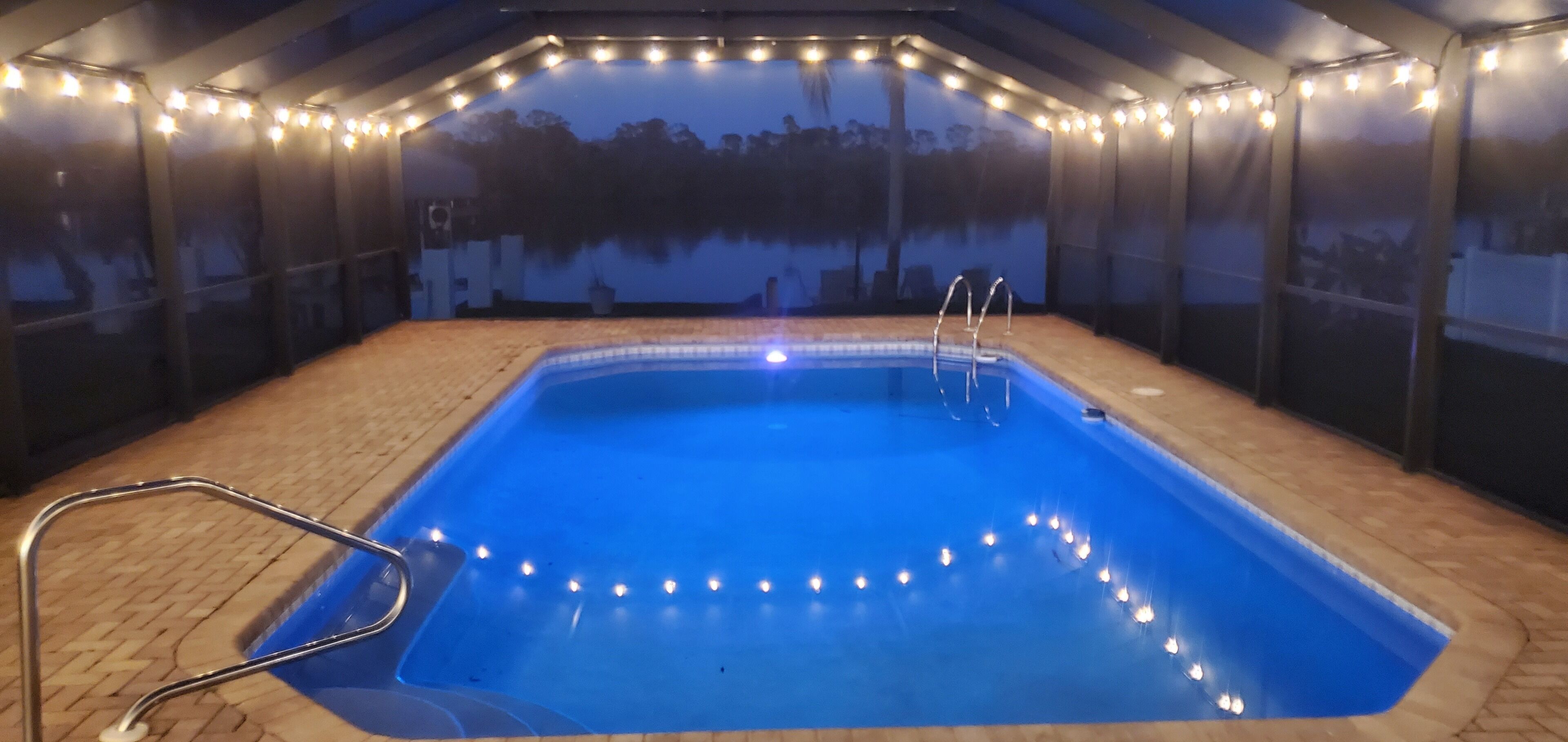Une piscine offrant une vue dégagée sur l’eau, entourée d’une zone abritée d’où l’on peut admirer les arbres, le tout délimité par une clôture.