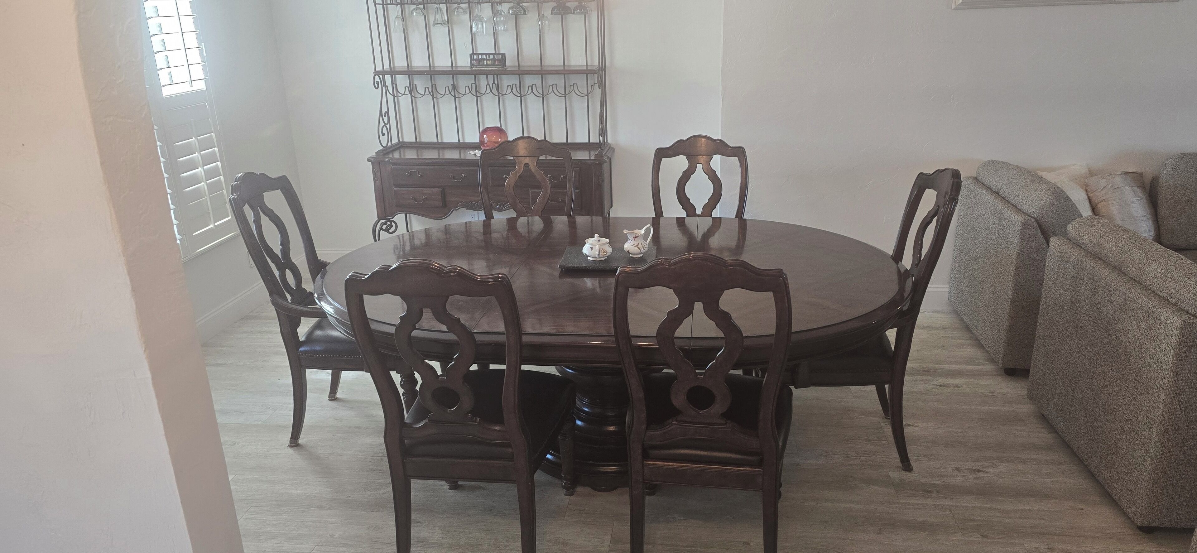 A dining area with a round wooden table and six chairs, a sofa, and a decorative cabinet in the background.