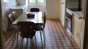 Een keuken met een zwart-witte vloer, een eettafel met stoelen, een raam met zonwering en een koelkast.