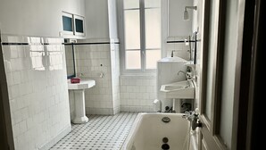 Een badkamer met een witte badkuip, een raam met uitzicht en een betegelde vloer.