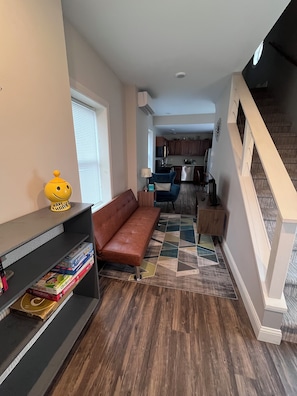 A compact living space with a sofa, a bookshelf, and a kitchen area in the background. - Tiny Home, Spa Next Door, Deck, Walk to Farmers Market (Dubuque)
