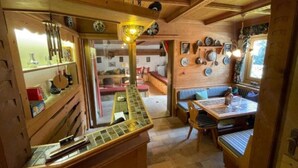 Un intérieur chaleureux, avec des éléments en bois, comprenant un coin repas, un banc et un mur décoré d’assiettes et d’ustensiles.