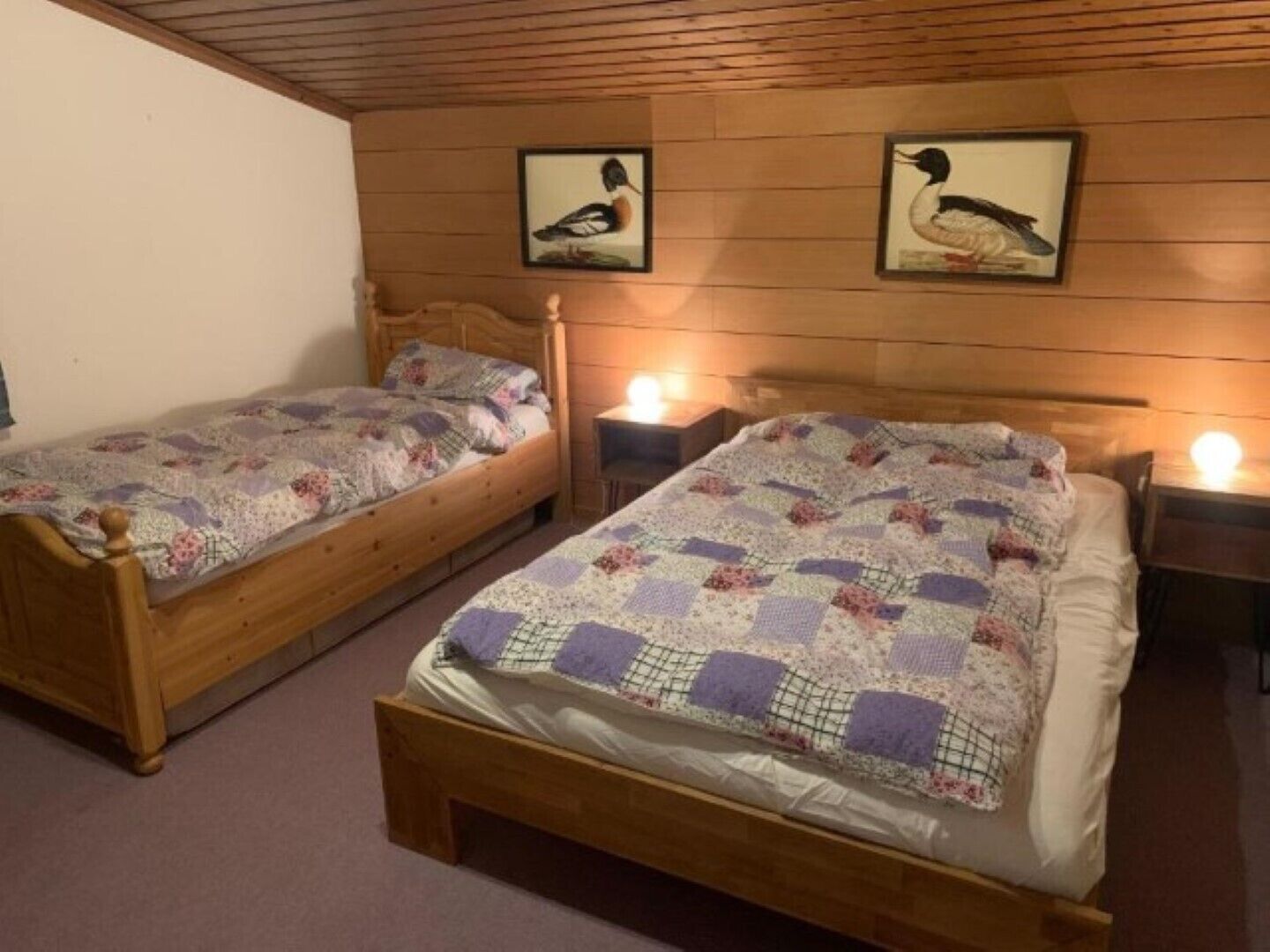 Two wooden beds with floral quilts, wooden headboards, and framed wall art of birds.