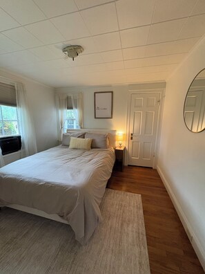 Una camera da letto con un letto, un comodino, una lampada, una finestra e un quadro appeso al muro.