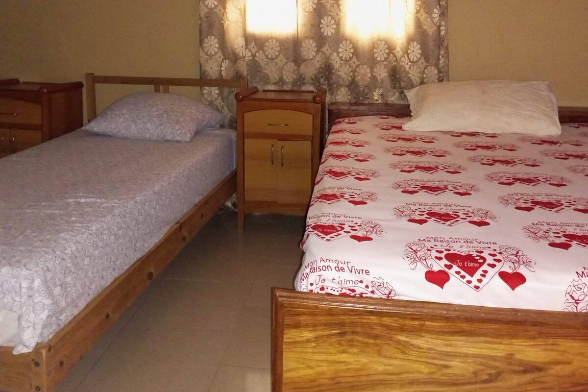 Een slaapkamer met twee eenpersoonsbedden, een houten nachtkastje en een raam met gordijnen met een patroon.