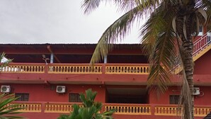 A multi-story building with a red facade, balconies with yellow railings, and a palm tree in the foreground. - Darsalam (Kedougou)