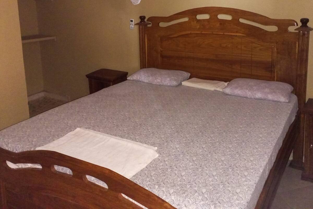 Een bed met een houten hoofdbord, een nachtkastje en een hangende lamp.