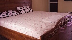 A wooden bed with a floral bedspread and two polka-dotted pillows. - Darsalam (Kedougou)