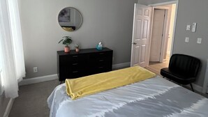 A bedroom with a bed, a dresser, a chair, a mirror, and a door.