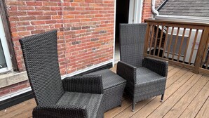 A wooden deck with wicker furniture and a brick wall.