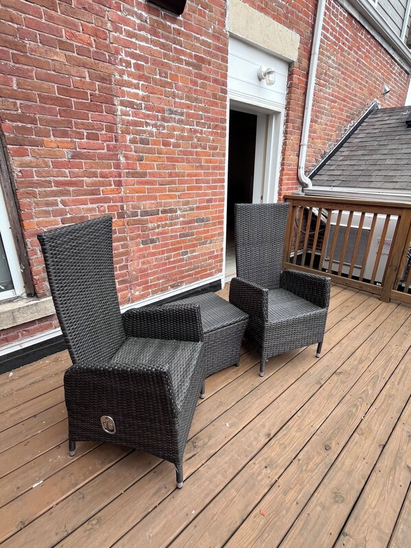 A wooden deck with wicker furniture and a brick wall.