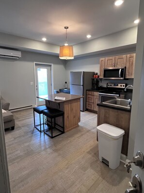 A modern kitchen with a central island, wooden cabinets, stainless steel appliances, and a pendant light.