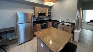 A modern kitchen with granite countertops, stainless steel appliances, wooden cabinets, and a pendant light.