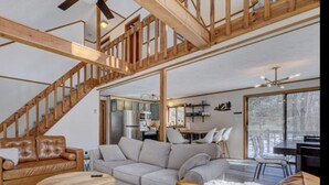 Een ruime woonkamer met een houten trap, een bank, een eettafel en een keuken op de achtergrond.