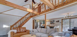 A spacious living area with a wooden staircase, a sofa, a dining table, and a kitchen in the background.