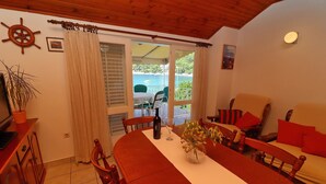Zona pranzo con tavolo in legno, sedie e vista sul mare attraverso una porta aperta.