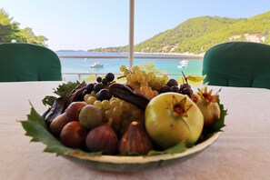 A table with a fruit and nut platter, a view of a coastal area with boats, and green chairs. - Apartment Star Day - Three Bedroom Apartment with Sea View (Prižba)