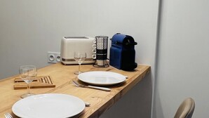 Un coin repas avec une table en bois, deux assiettes, un verre, un grille-pain, une machine à café et une chaise.