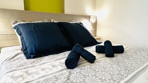 Un lit bien fait, avec une couvre-lit à motifs, deux oreillers foncés et des serviettes enroulées.